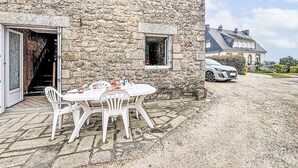 A stone building with a patio table and chairs, a car parked nearby, and a staircase leading to an upper level. - Maison Le Magouër by Interhome (Plouhinec Morbihan)