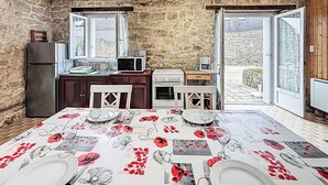 A kitchen with a stone wall, a refrigerator, a microwave, a stove, and a dining table set with plates and glasses. - Maison Le Magouër by Interhome (Plouhinec Morbihan)