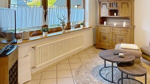 A room with a large window, a radiator, a wooden cabinet, a sofa, and a small round table. - Sommer Apartements Schwarzwald by Interhome (Simonswald)