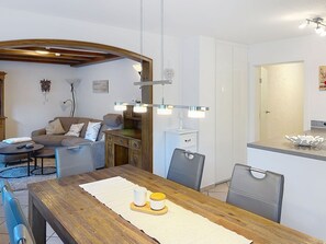 A modern living room with a wooden dining table, grey sofa, and a kitchen area with white cabinets. - Sommer Apartements Schwarzwald by Interhome (Simonswald)
