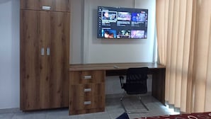 A room with a wooden desk, a TV mounted on the wall, a chair, and a wardrobe.