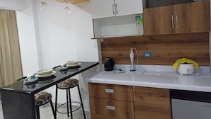 A compact kitchen with a black countertop, wooden cabinets, a white sink, and a small bar area with stools.