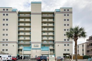 A multi-story hotel with a central entrance, balconies on each floor, and a parking area in front. - Oceanfront condo with private balcony, indoor pool & direct beach access (North Myrtle Beach)