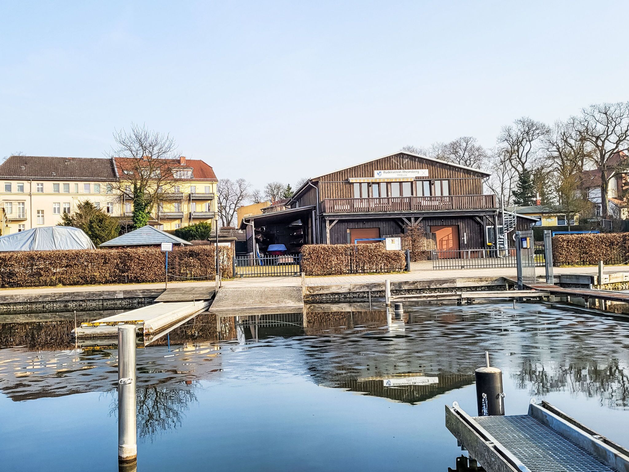 A waterfront building with a dock, a covered area, and a reflection in the water.