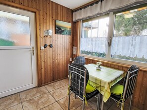 A room with wooden panel walls, a window with a view of a building and trees, a table with a green tablecloth, and a chair with a yellow cushion.