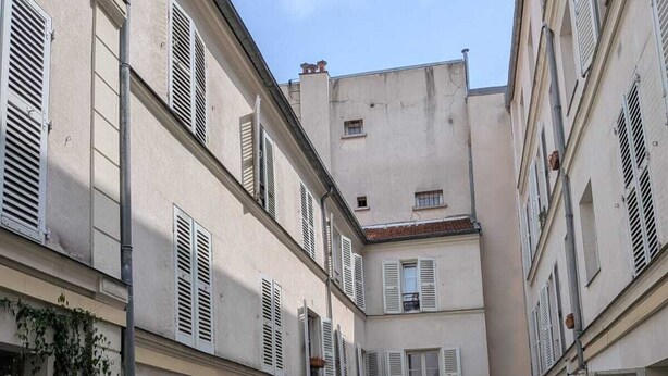 Ein Innenhof mit Pflastersteinen, Blumentöpfen und Gebäuden mit Fensterläden.