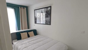 Ein Schlafzimmer mit einem Bett, einem Fenster mit Vorhängen, einem Wandbild und einem Fliesenboden.