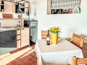 Una cocina compacta con comedor, un refrigerador pequeño, un microondas y una mesa de comedor con un florero.