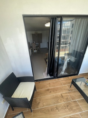 A balcony with a wicker chair, a small table, and a view into a dining area. - Luxury Hotel style Apartment. With a/c, hot and cold water. 3bs 2 bathroom  (Santo Domingo Este)
