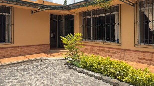Un edificio residencial con un porche cubierto, un pequeño jardín y base de ladrillo.