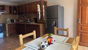 Una cocina con armarios de madera, un refrigerador, una mesa de comedor con sillas y un pequeño adorno en la mesa.