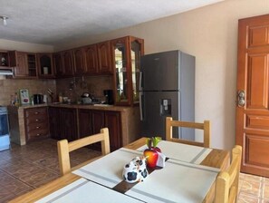 A kitchen with wooden cabinets, a refrigerator, a dining table with chairs, and a small decorative item on the table.