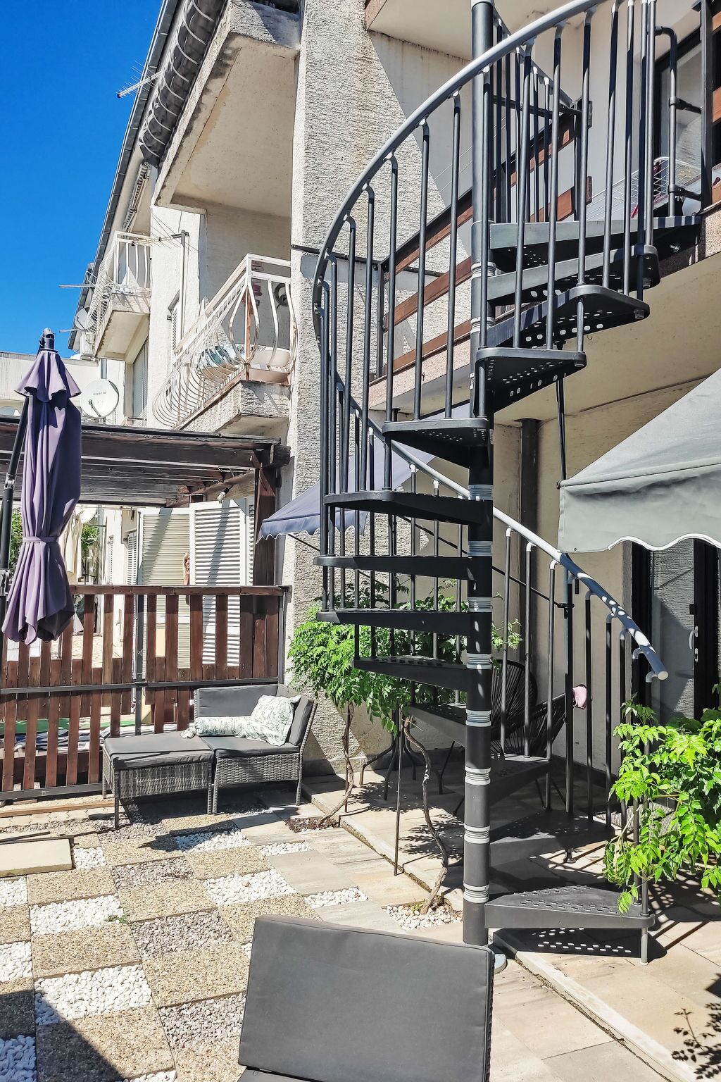 Ein Wohngebäude mit einer Wendeltreppe, Sitzgelegenheiten im Freien und einem umzäunten Patio.