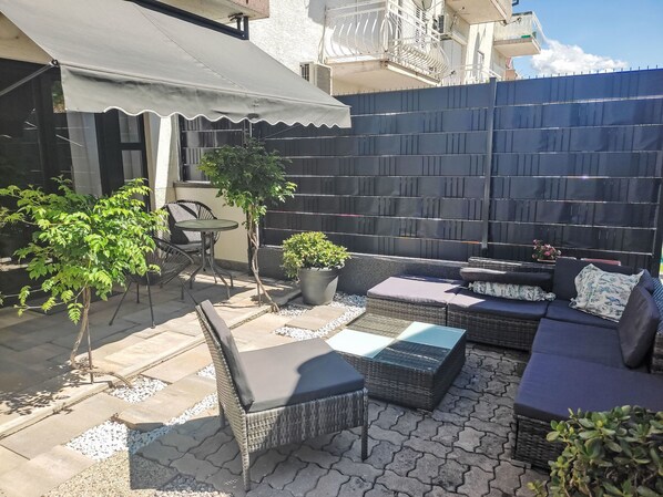 Eine Terrasse mit Korbmöbeln, einem kleinen Tisch und Topfpflanzen.