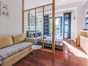 A modern living room with a sofa, a small white table, a bed with a wooden headboard, and a sliding glass door leading to a balcony. - Vacation home Deleut by Interhome (Novi Vinodolski)