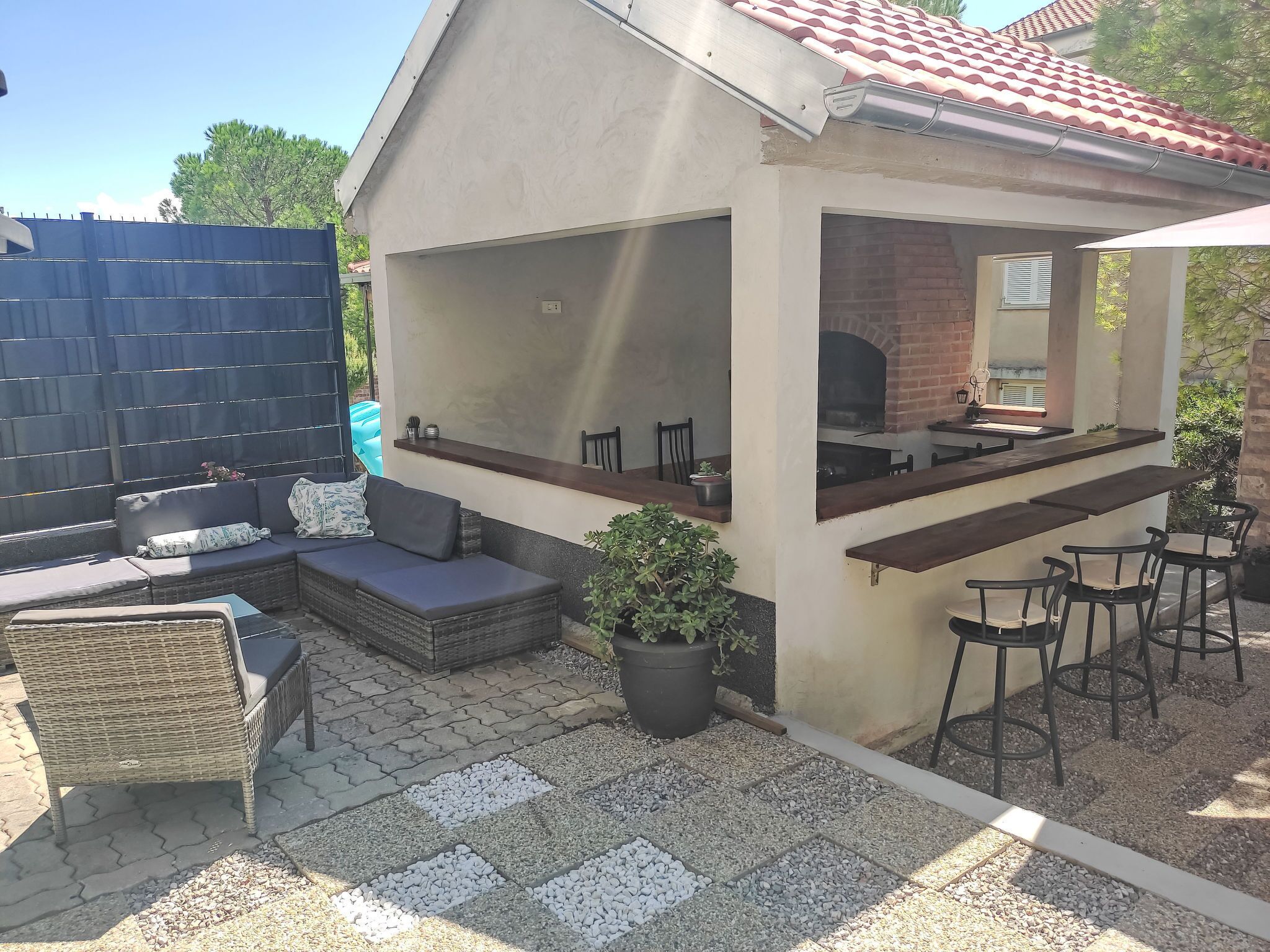 Un patio exterior con zona de estar, una parrilla y una planta en maceta.
