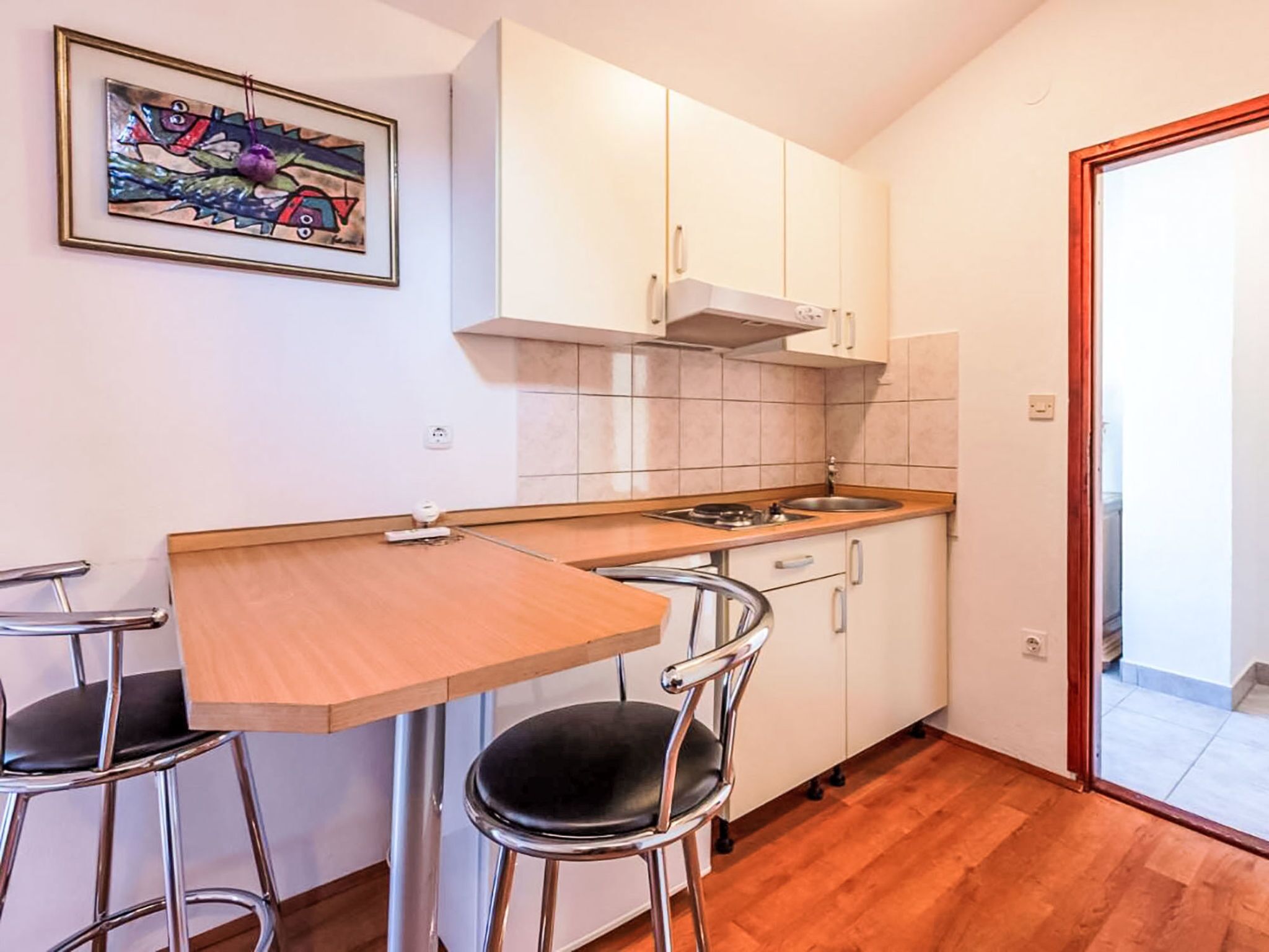 Una cocina compacta con una mesa de madera, dos taburetes de bar, armarios blancos y un salpicadero de azulejos.