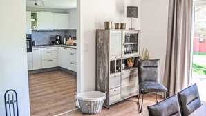 Una cocina moderna con armarios blancos, una zona de comedor con una silla y una mesa, y piso de madera.