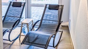 Un solarium con dos sillones reclinables, ventanas amplias y vistas a un edificio de ladrillo y follaje.