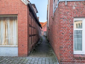 Ein schmaler Gang zwischen roten Backsteingebäuden mit großen Fenstern und einem Ziegeldach.