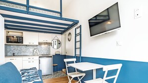 Un espacio habitable compacto con kitchenette, una zona de comedor con mesa y sillas, un sofá y un televisor montado en la pared.