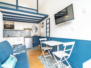 Ein kompakter Wohnbereich mit Küchenzeile, einer Essecke mit Tisch und Stühlen, einer Sitzecke und einem an der Wand befestigten Fernseher.