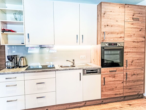 A modern kitchen with white cabinets, a wooden accent wall, a built-in oven, and a coffee maker.