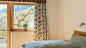 A bedroom with a bed, a window with curtains, a plant, and a view of a stone wall. - Josephine by Interhome (Auffach)