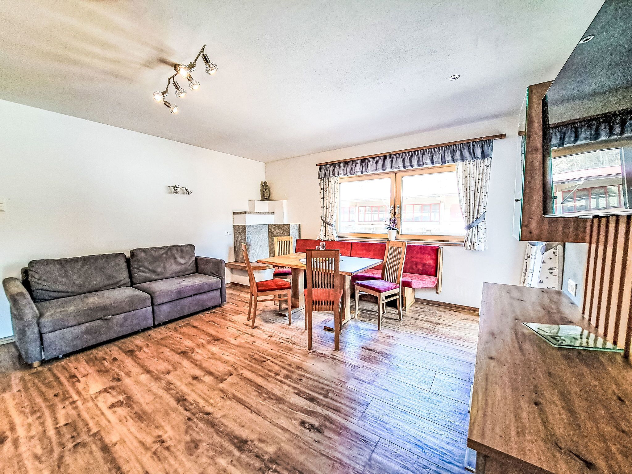 Een woonkamer met een bank, een eettafel met stoelen, een raam met gordijnen en een plafondlamp.
