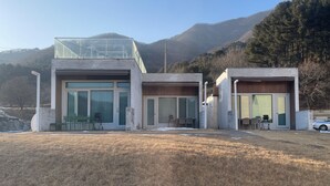 Una casa moderna con balcón de cristal, amplias ventanas y vistas a las montañas.