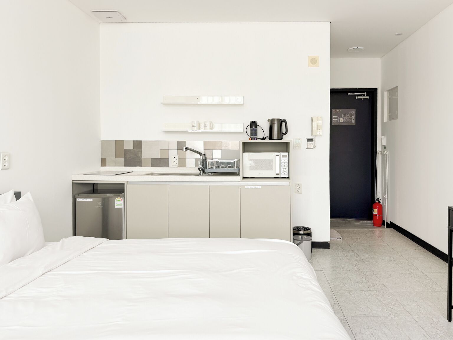 A hotel room with a bed, kitchenette, and a door leading to the hallway.
