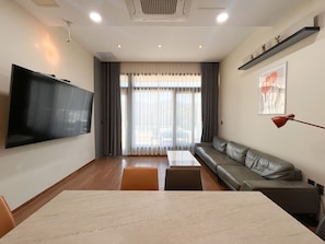 A modern living room with a flat-screen TV, a sofa, a coffee table, and a dining table.