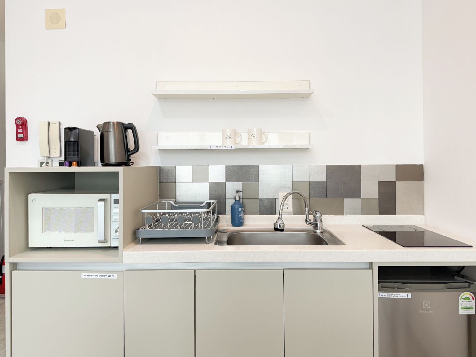A compact kitchen with a microwave, coffee maker, kettle, and a dish rack.