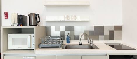A compact kitchen with a microwave, coffee maker, kettle, and a dish rack.