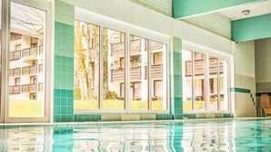A swimming pool with clear water, surrounded by large windows with views of trees and a building. - im Schlosspark mit Hallenbad by Interhome (Lofer)