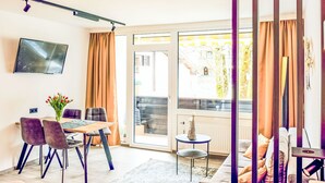 A modern living room with a dining area, a TV mounted on the wall, and a sliding glass door leading to an outdoor area. - im Schlosspark mit Hallenbad by Interhome (Lofer)