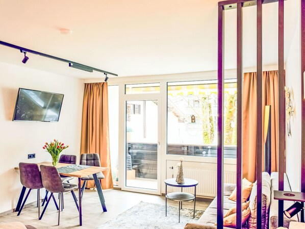 A modern living room with a dining area, a TV mounted on the wall, and a sliding glass door leading to an outdoor area. - Grubhof by Interhome (Lofer)