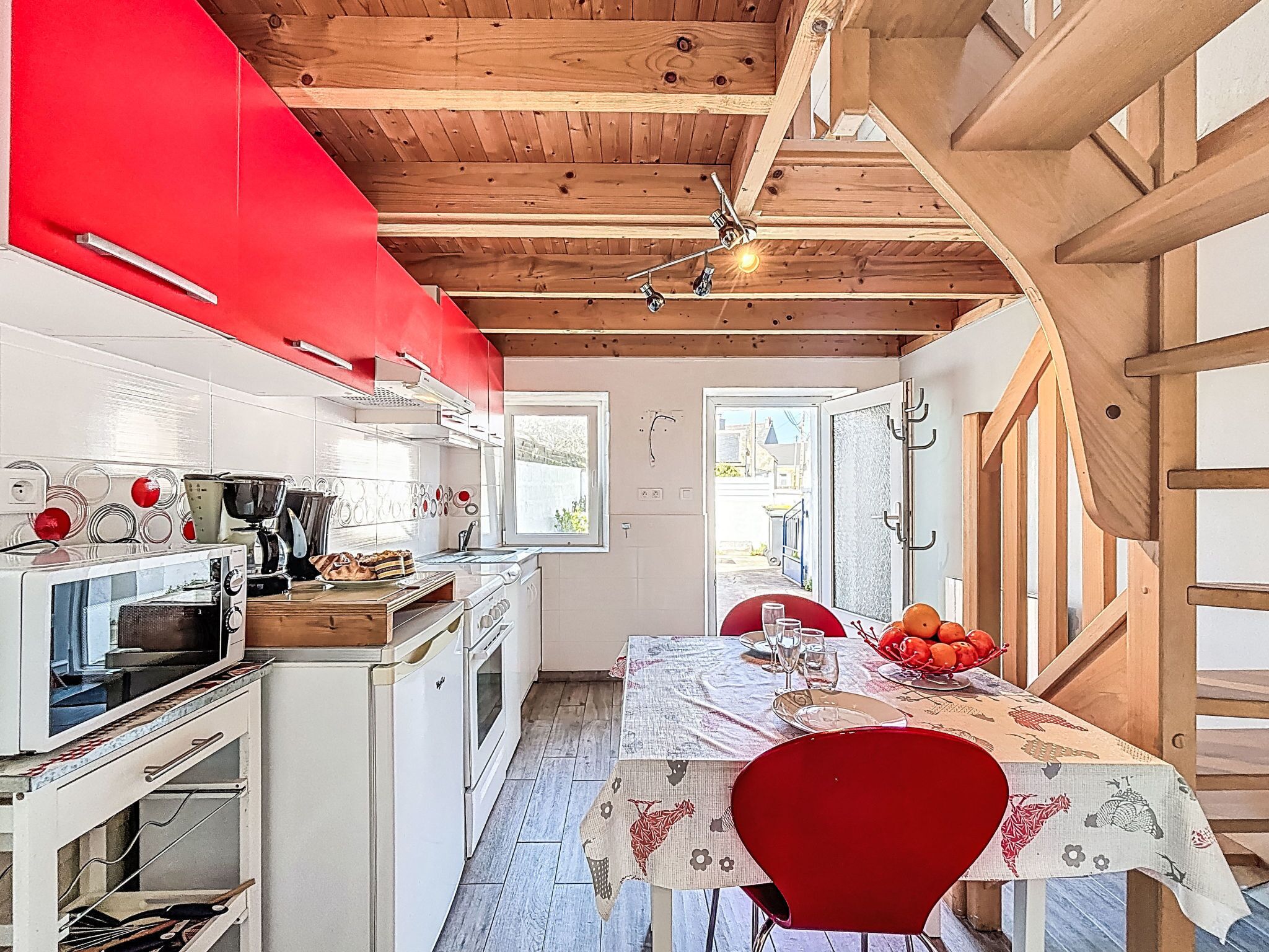 A kitchen with white cabinets, a red upper section, and a dining area with a table set for two.