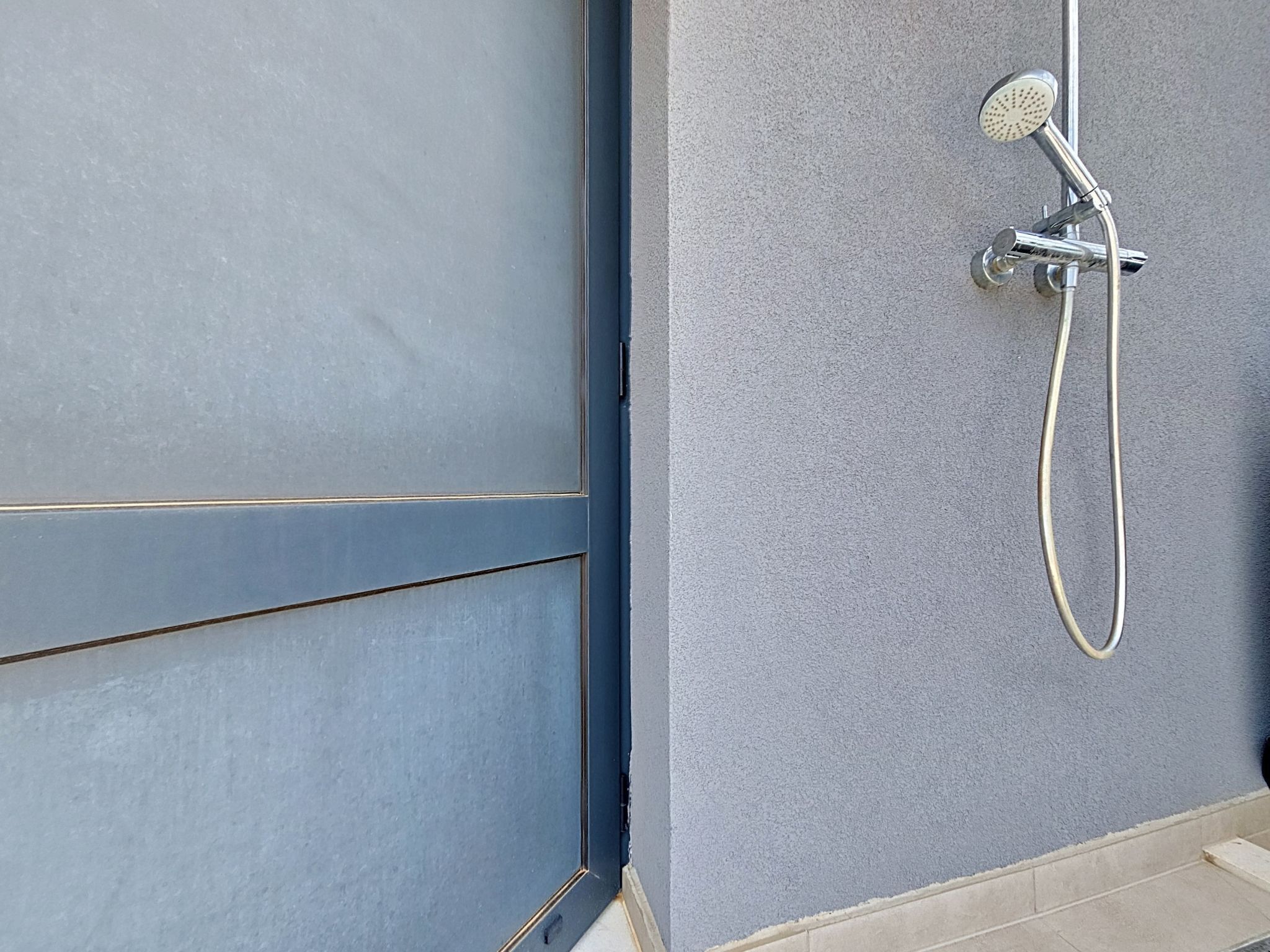 A shower with a handheld showerhead and a hose, mounted on a textured wall.