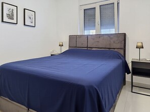 A bedroom with a large bed, two bedside tables, a window with blinds, and two framed pictures on the wall. - Sunny Terrace by Interhome (Trogir/Okrug Gornji)