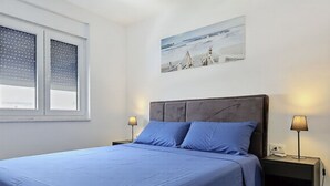 Ein Schlafzimmer mit einem Bett, zwei Nachttischen, einem Fenster mit Jalousien und einem Wandbild.
