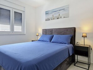 Ein Schlafzimmer mit einem Bett, zwei Nachttischen, einem Fenster mit Jalousien und einem Wandbild.