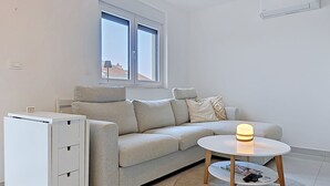 Ein modernes Wohnzimmer mit einer Couch, einem kleinen Tisch, einem Schrank und einem Fenster.