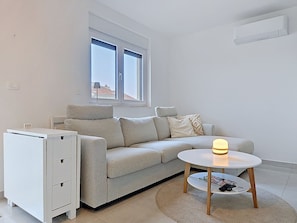 Ein modernes Wohnzimmer mit einer Couch, einem kleinen Tisch, einem Schrank und einem Fenster.