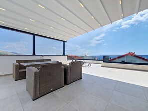 A rooftop terrace with wicker furniture, large windows, and a view of the sea. - Sunny Terrace II by Interhome (Trogir/Okrug Gornji)