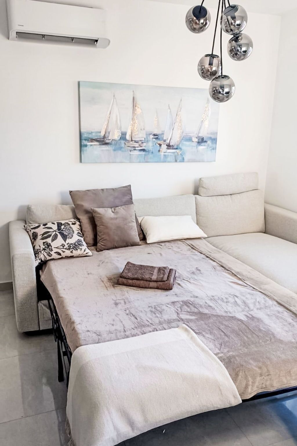 A modern living room with a sofa, a coffee table, and a painting of sailboats.