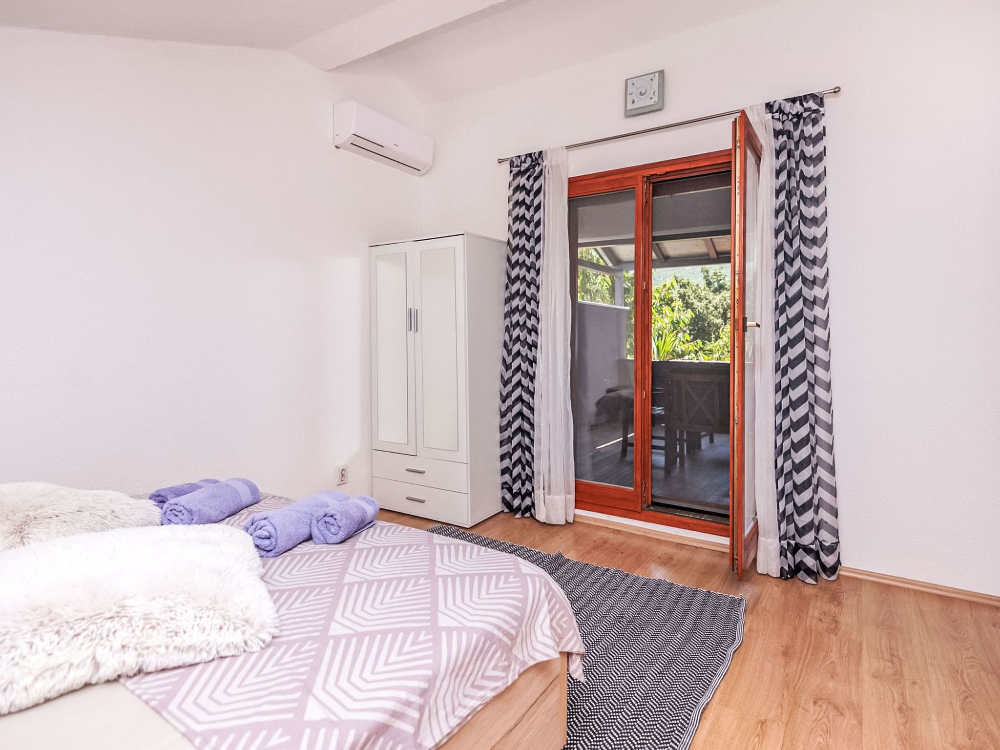 Quarto com cama, guarda-roupa, porta de vidro deslizante para uma varanda e ventoinha no teto.