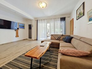 Un salon comprenant un canapé, une table basse en bois, un téléviseur à écran plat et une fenêtre avec des rideaux.