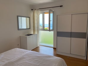 A bedroom with a bed, a wardrobe, a mirror, a window with curtains, and a view of the sea. - mit Terrasse by Interhome (Rab/Supetarska Draga)