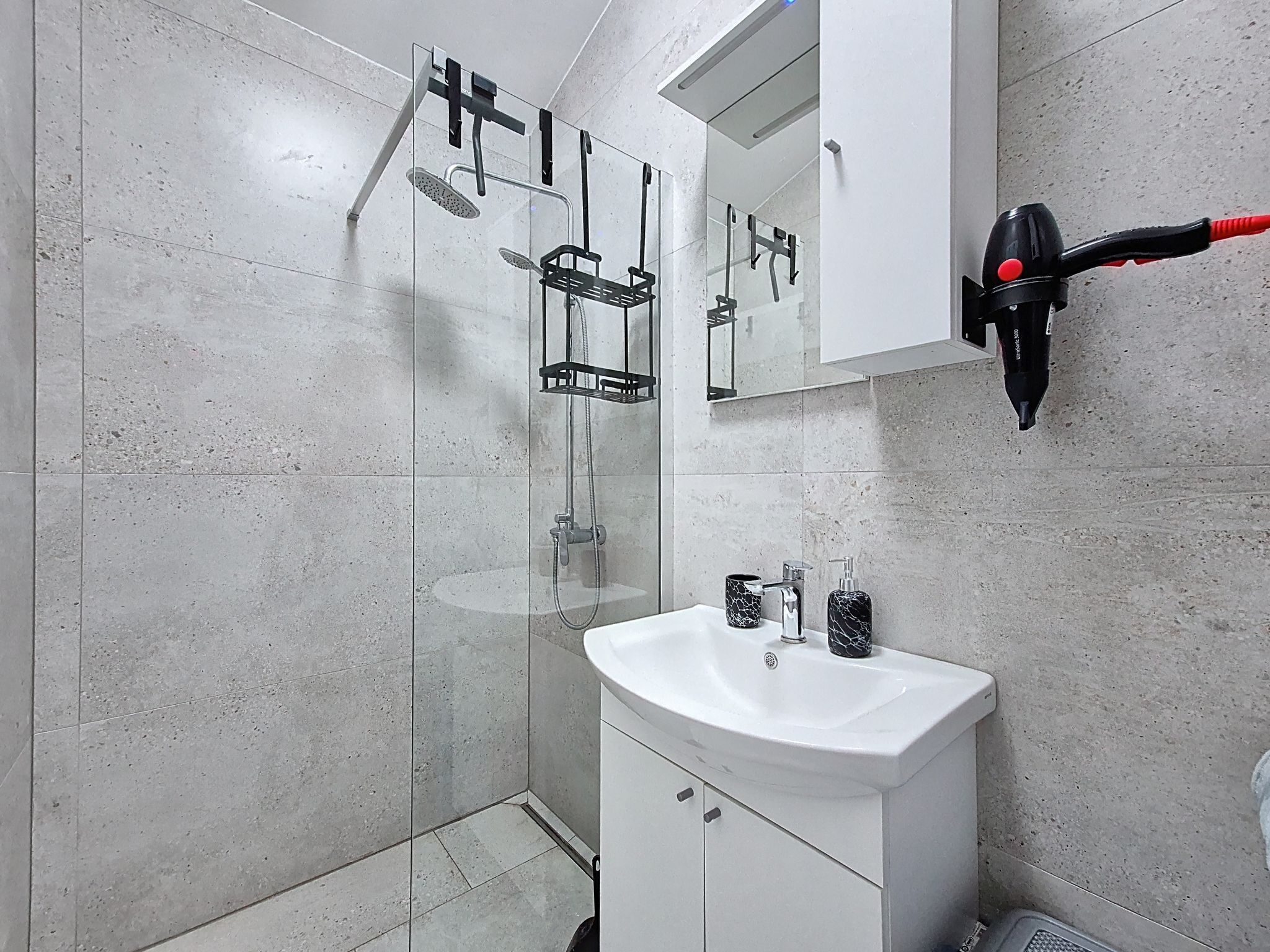 Une salle de bain moderne avec une douche à parois de verre, un lavabo blanc et un sèche-cheveux fixé au mur.